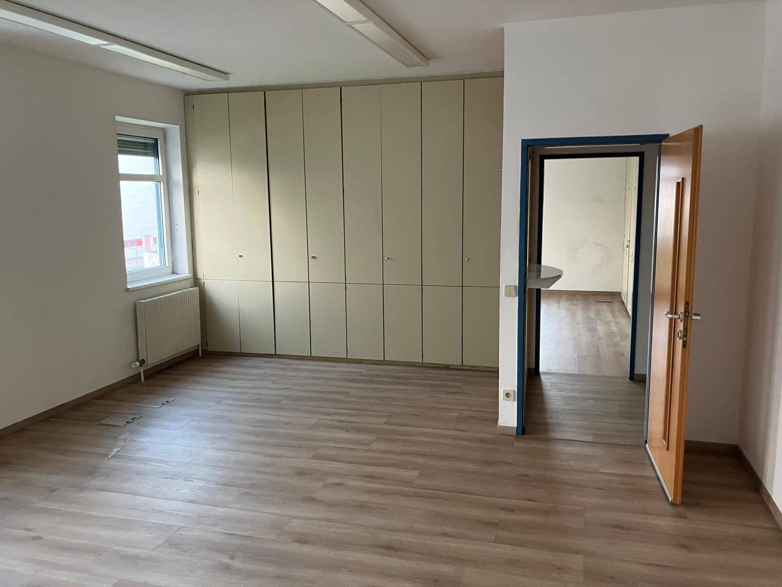 Büroraum mit integrierten Schränken und einem offenen Durchgang zu einem weiteren Bereich, mit Laminatboden.
