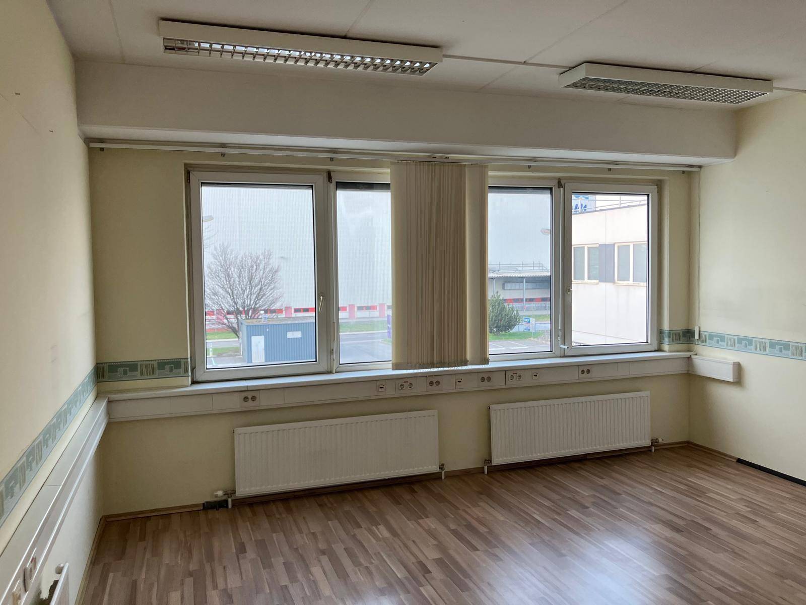 Geräumiges Büro mit Laminatboden, großen Fenstern und Deckenleuchten, bereit zur Nutzung mit Stadtblick.