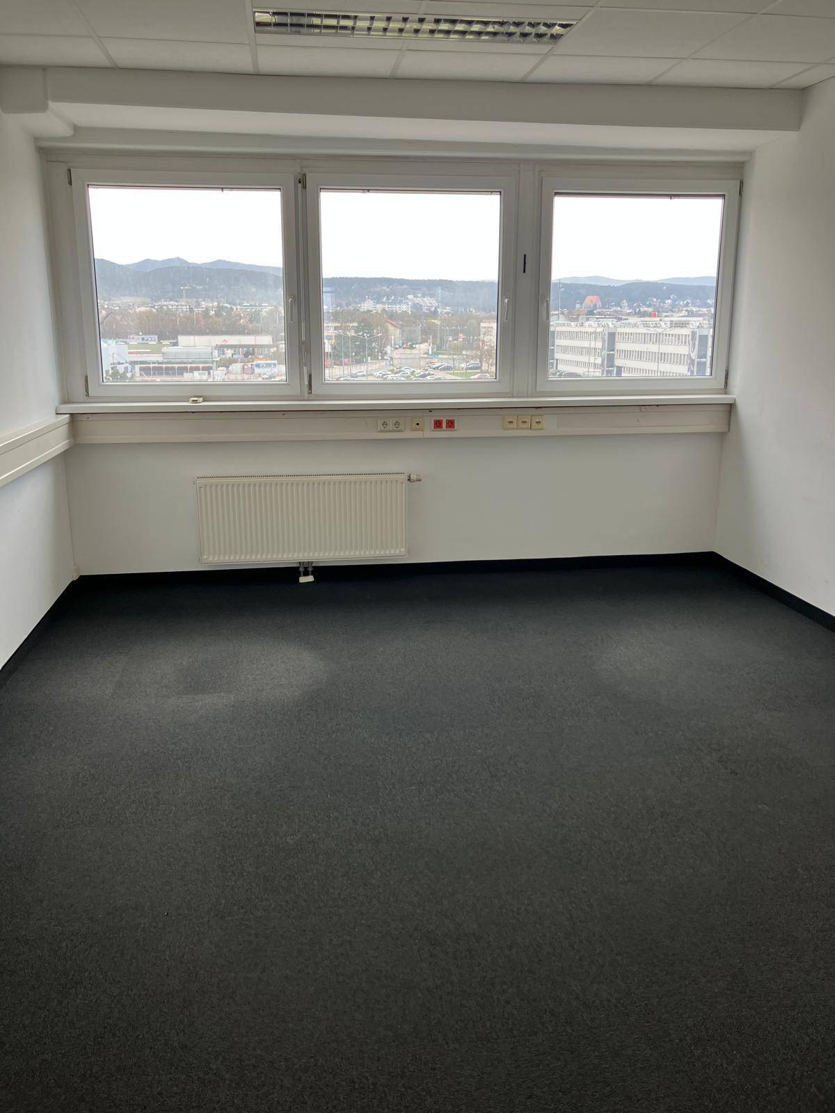 Helles Büro mit weitem Blick auf die Stadt und die umliegende Landschaft, ausgestattet mit dunklem Teppichboden.