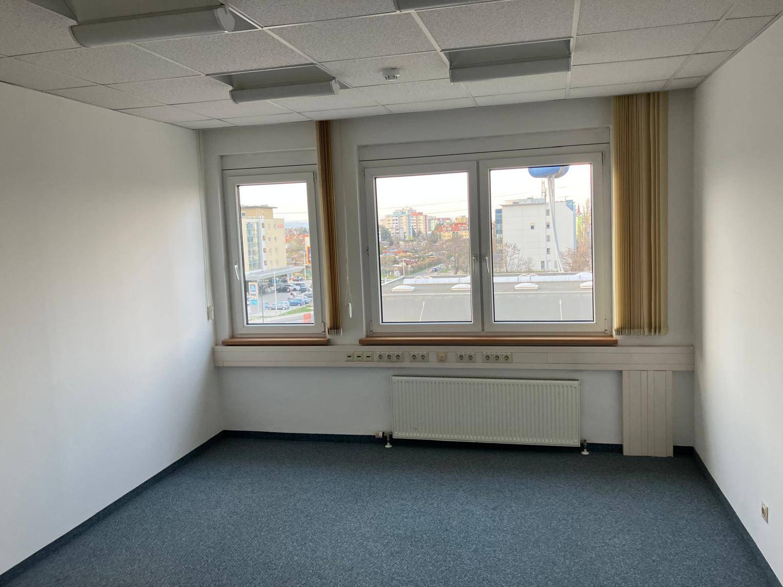 Geräumiger Büroraum mit Teppichboden, Heizkörpern und großen Fenstern mit Stadtblick.