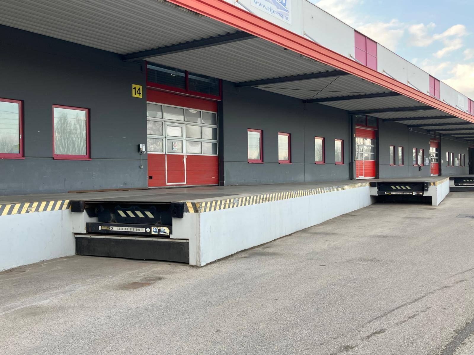 Lange Reihe von Laderampen an einer modernen Industriehalle mit roten Akzenten und breiter Zufahrt.