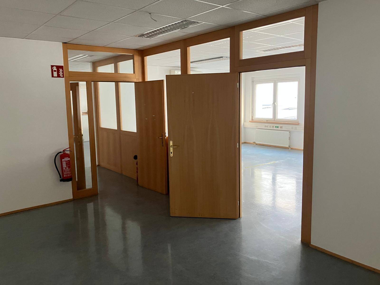 Eingangsbereich zu einem Bürobereich mit Feuerlöscher und Blick in mehrere Räume.