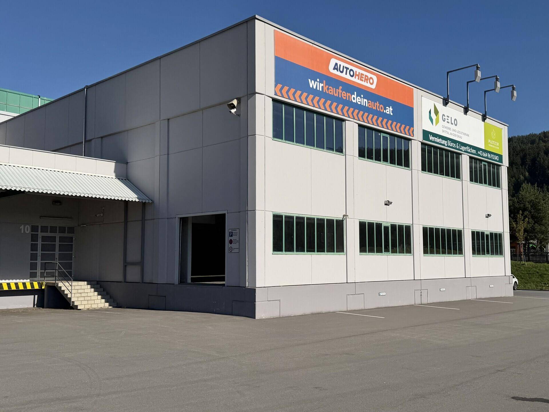 Moderne Gewerbeimmobilie mit großen Fenstern, Laderampe und Werbeschildern an der Fassade.