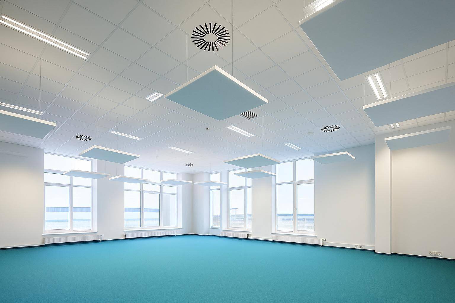Heller, moderner Büroraum mit großen Fenstern, Akustikdeckenplatten und blauem Vinylboden.