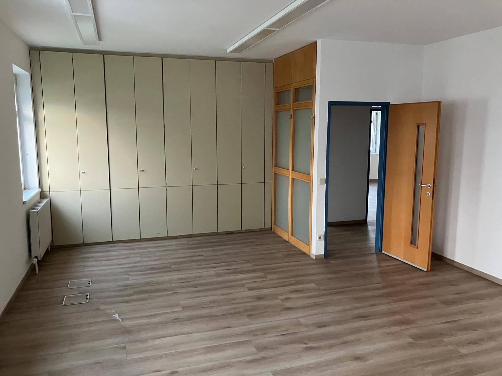 Geräumiger Büroraum mit integrierten Schränken, einer Holztür und einem weiteren Durchgang, mit Laminatboden.