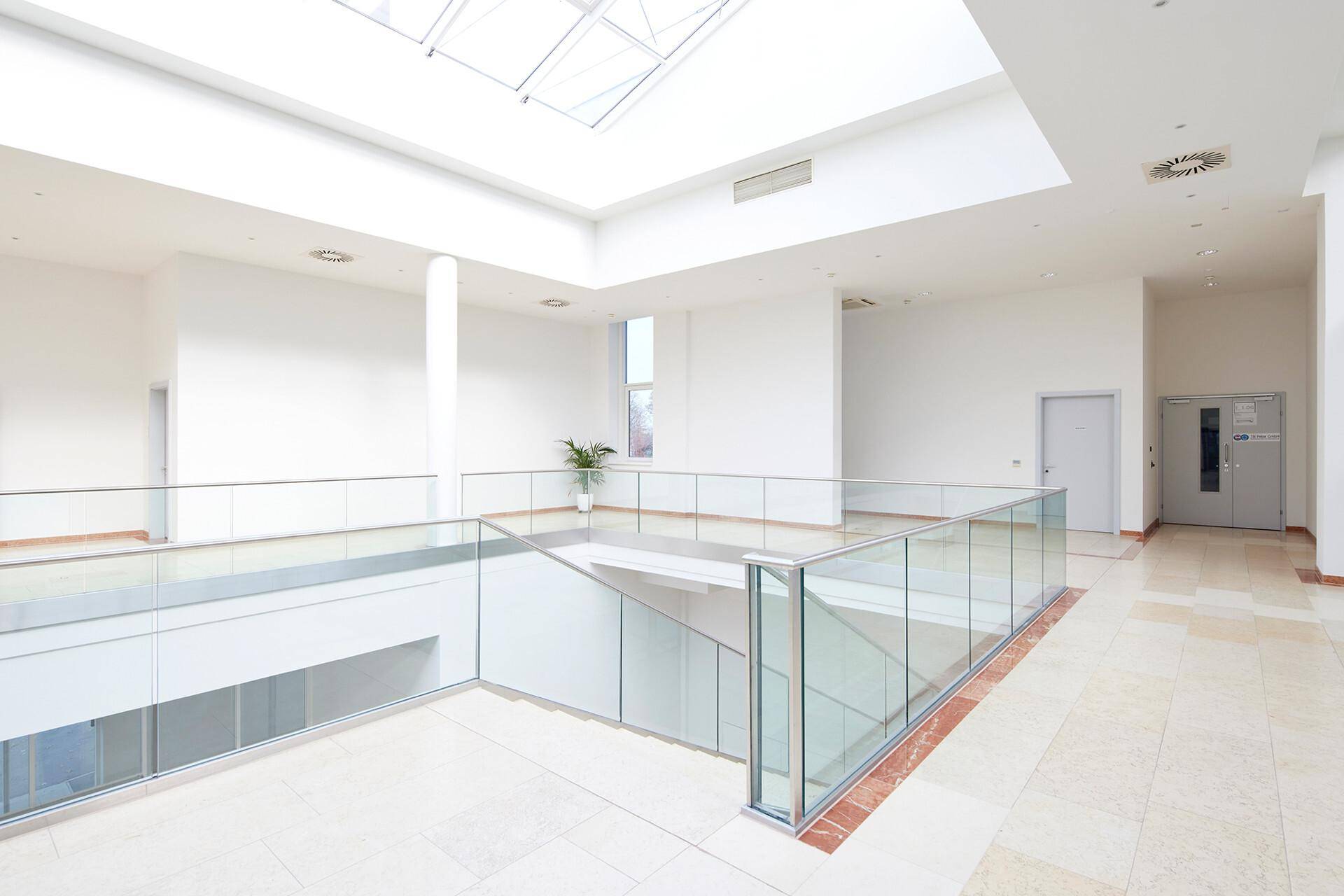 Heller Flur im Obergeschoss mit Glasgeländern, Blick auf die Lobby und viel Tageslicht durch das Oberlicht.