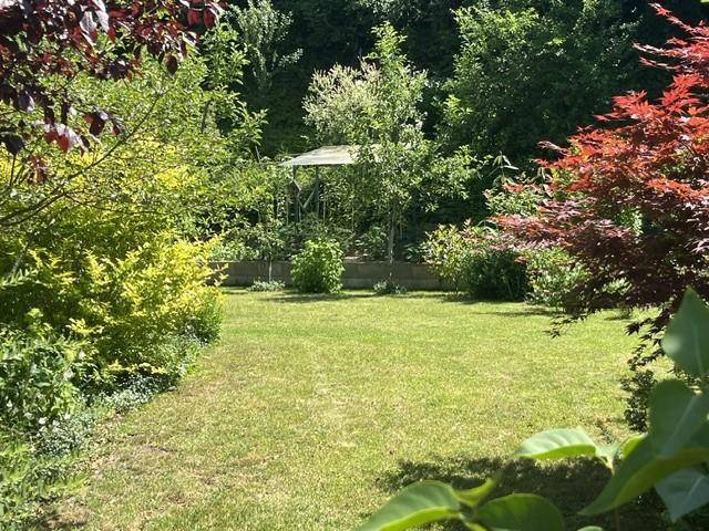 Gepflegter Garten mit Rasenfläche, verschiedenen Bäumen und Sträuchern in voller Blüte.