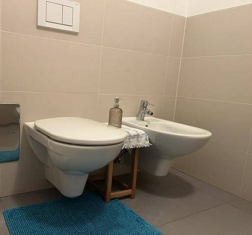 Modernes Gäste-WC mit Wand-WC, Bidet und hellen Fliesen am Boden und an den Wänden.