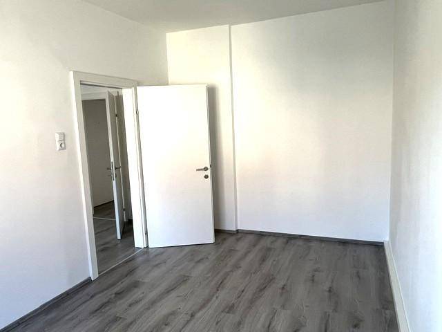 Helles Zimmer mit weiß gestrichenen Wänden und dunklem Laminatboden, bereit zur Einrichtung.