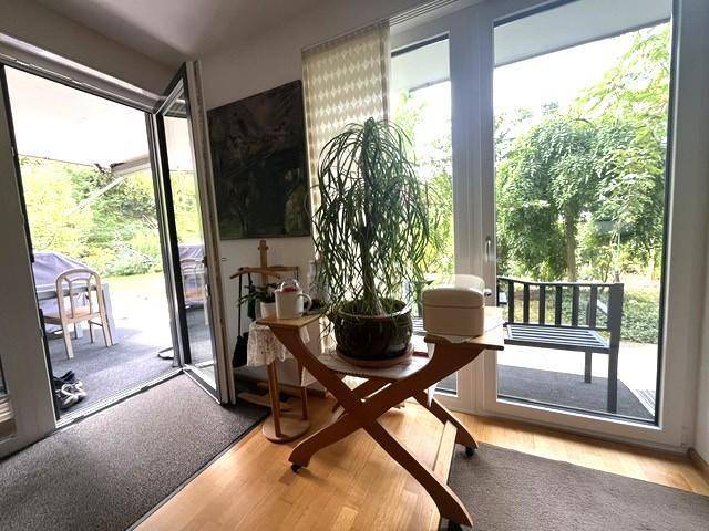 Heller Innenbereich mit Holzboden und großen Fenstern, die Zugang zu einer möblierten Terrasse bieten.