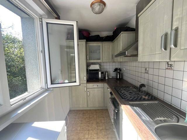 Kleine Küche mit Fenster, hellen Schränken, Fliesenrückwand und integrierten Geräten.