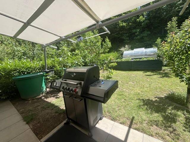 Überdachter Grillbereich im Garten mit Gasgrill und viel Grün im Hintergrund.