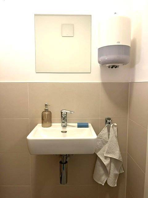 Kleines Waschbecken mit Spiegel und Seifenspender in einem modernen Gäste-WC.