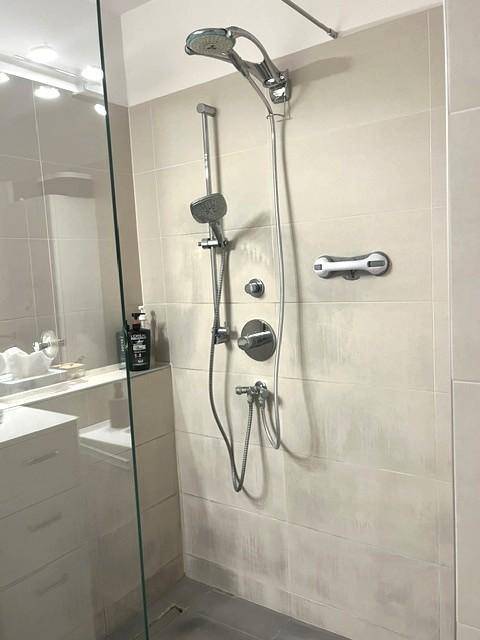 Modernes Badezimmer mit begehbarer Dusche, hellen Fliesen und praktischen Haltegriffen.