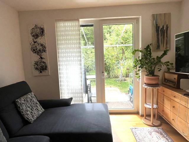 Gemütliches Wohnzimmer mit Sofa, Kommode und Blick in den grünen Garten.