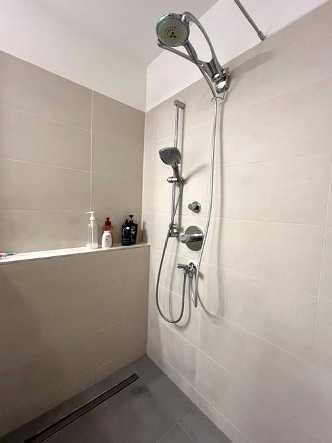Moderne Duschkabine mit Regendusche, Handbrause und hellen Fliesen in einem Badezimmer.