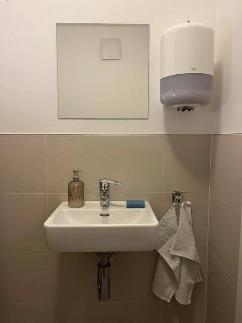 Kleines Gäste-WC mit modernem Waschbecken, Wandspiegel und hellen Fliesen.