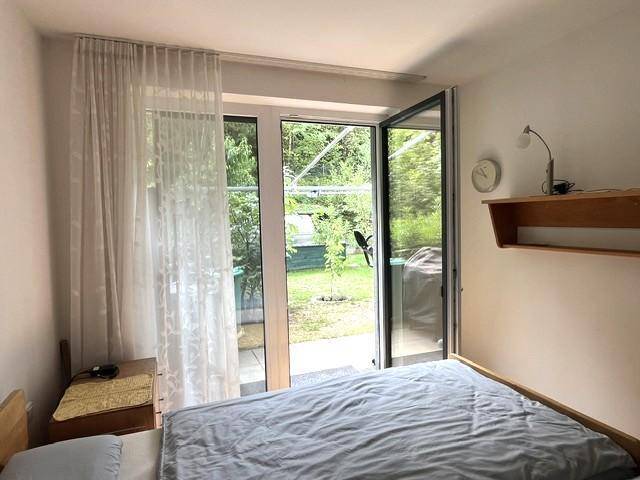 Schlafzimmer mit Bett, Nachttisch und direktem Zugang zum grünen Gartenbereich.