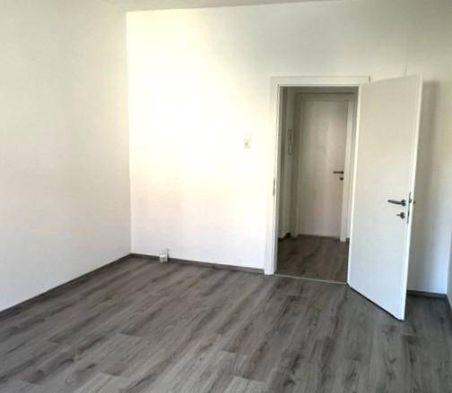 Leeres Zimmer mit Laminatboden und weiß gestrichenen Wänden, ideal für Schlaf- oder Arbeitszimmer.