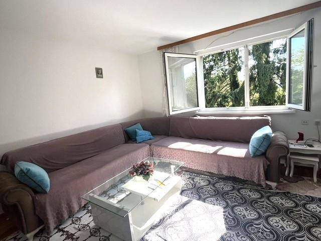 Helles Wohnzimmer mit großem Ecksofa, Couchtisch und Blick ins Grüne durch die Fenster.