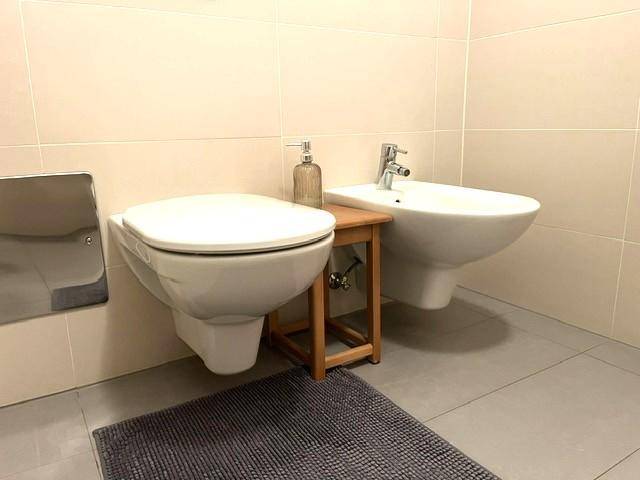 Helles Badezimmer mit wandhängender Toilette, Bidet und modernen Fliesen.