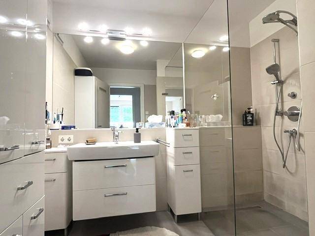 Helles Badezimmer mit modernem Waschtisch, großem Spiegelschrank und begehbarer Dusche.