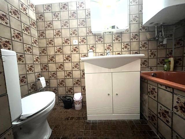 Badezimmer mit gemusterten Fliesen, Toilette, Waschbecken und Spiegelschrank.