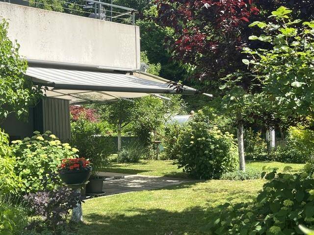 Sonnige Gartenterrasse mit Markise und üppiger Bepflanzung, ideal zum Entspannen.