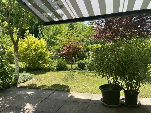 Geräumige Terrasse mit Markise und weitem Blick in den grünen, gepflegten Garten.