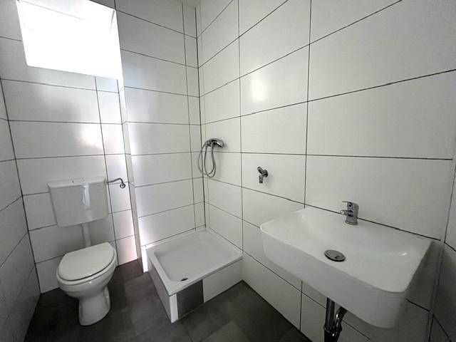 Helles Badezimmer mit weißen Fliesen, Dusche, WC und modernem Einzelwaschbecken.