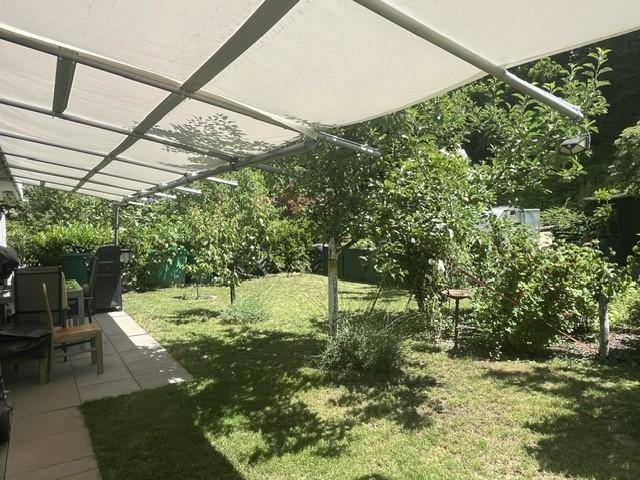 Weitläufiger Garten mit überdachtem Bereich und üppiger Vegetation unter blauem Himmel.