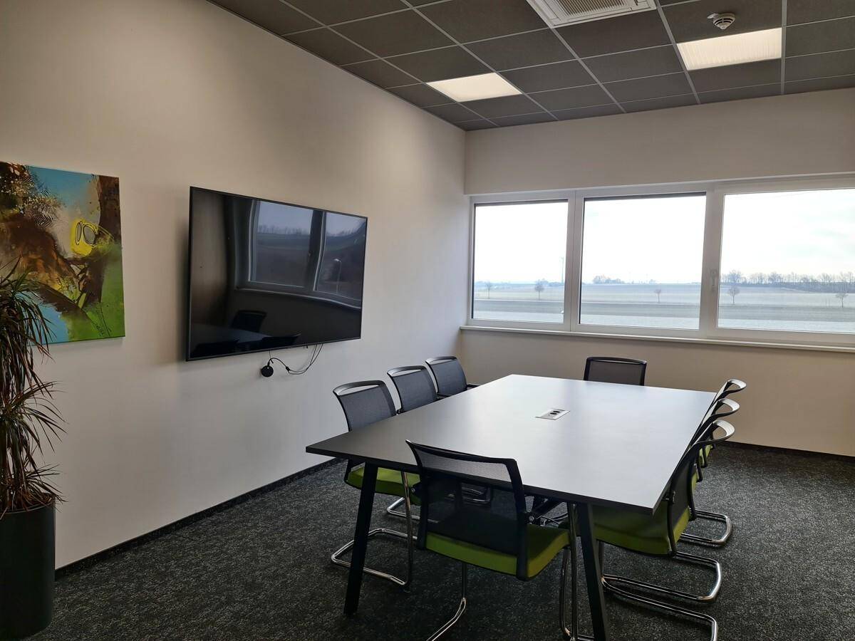 Moderner Konferenzraum mit großem Tisch, Bürostühlen, Wandfernseher und Fenstern, ideal für Besprechungen.