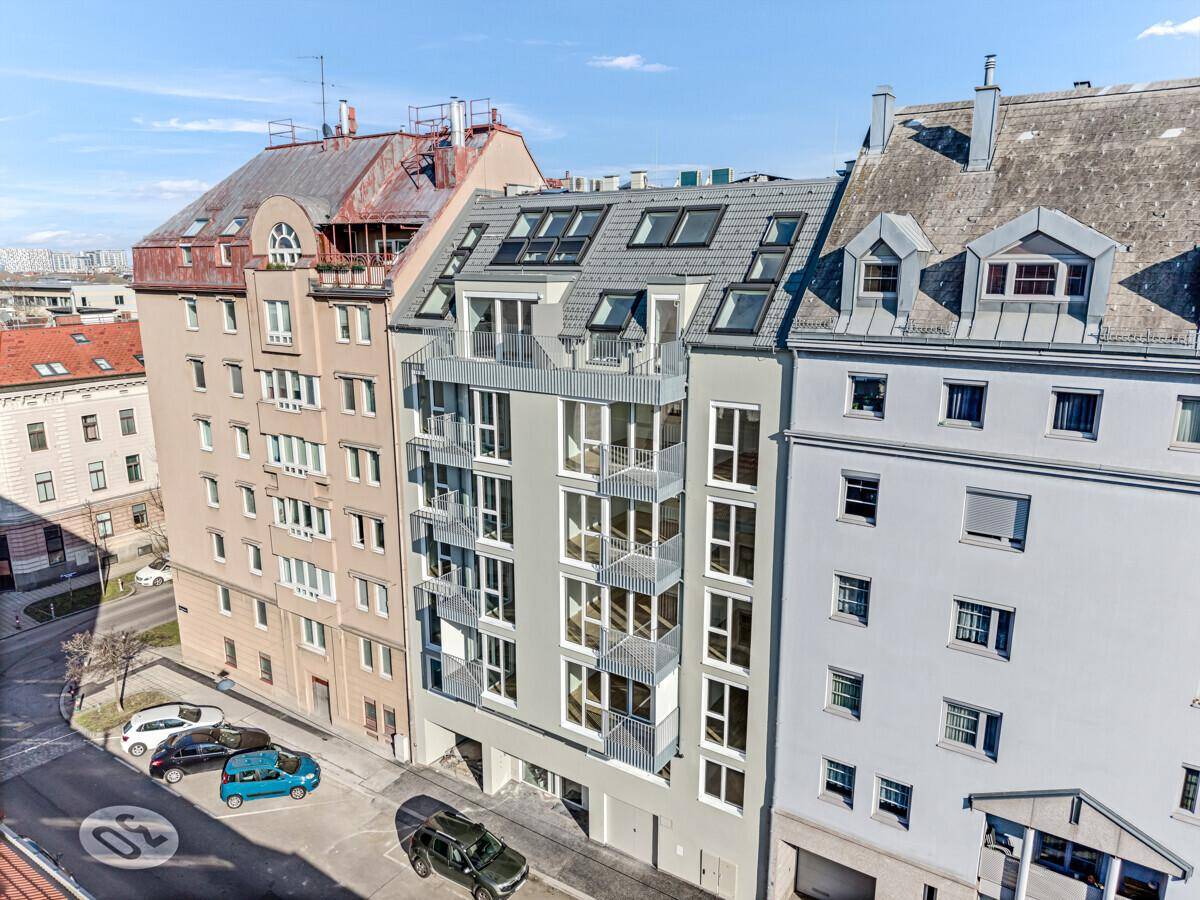 Moderne Fassade eines Wohngebäudes mit Balkonen und großen Fenstern, umgeben von älteren Gebäuden.