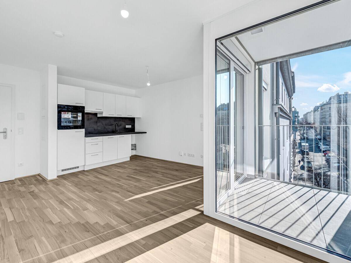 Offener Wohnbereich mit integrierter Küchenzeile, Holzboden und Zugang zu einem Balkon.