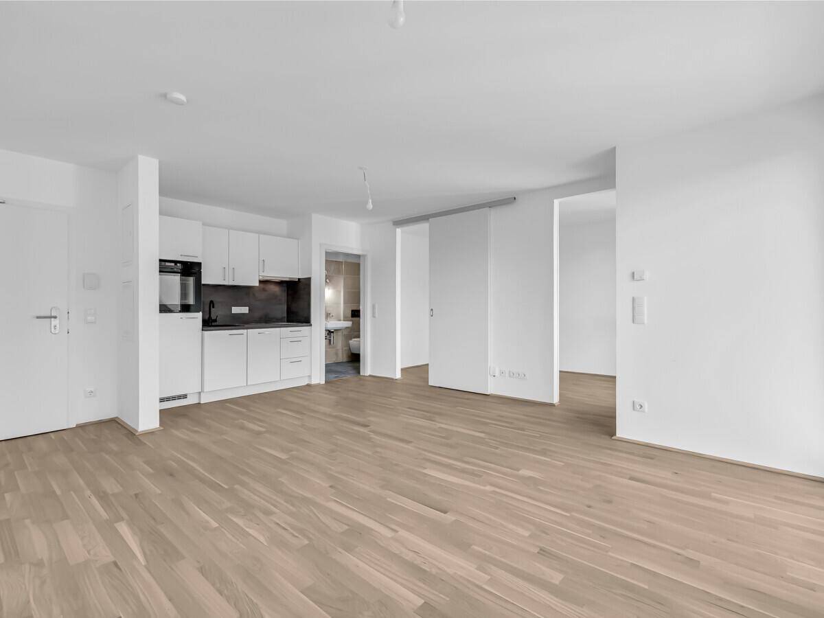 Offener Wohnbereich mit integrierter Küchenzeile und Holzboden, mit Blick auf ein Badezimmer.