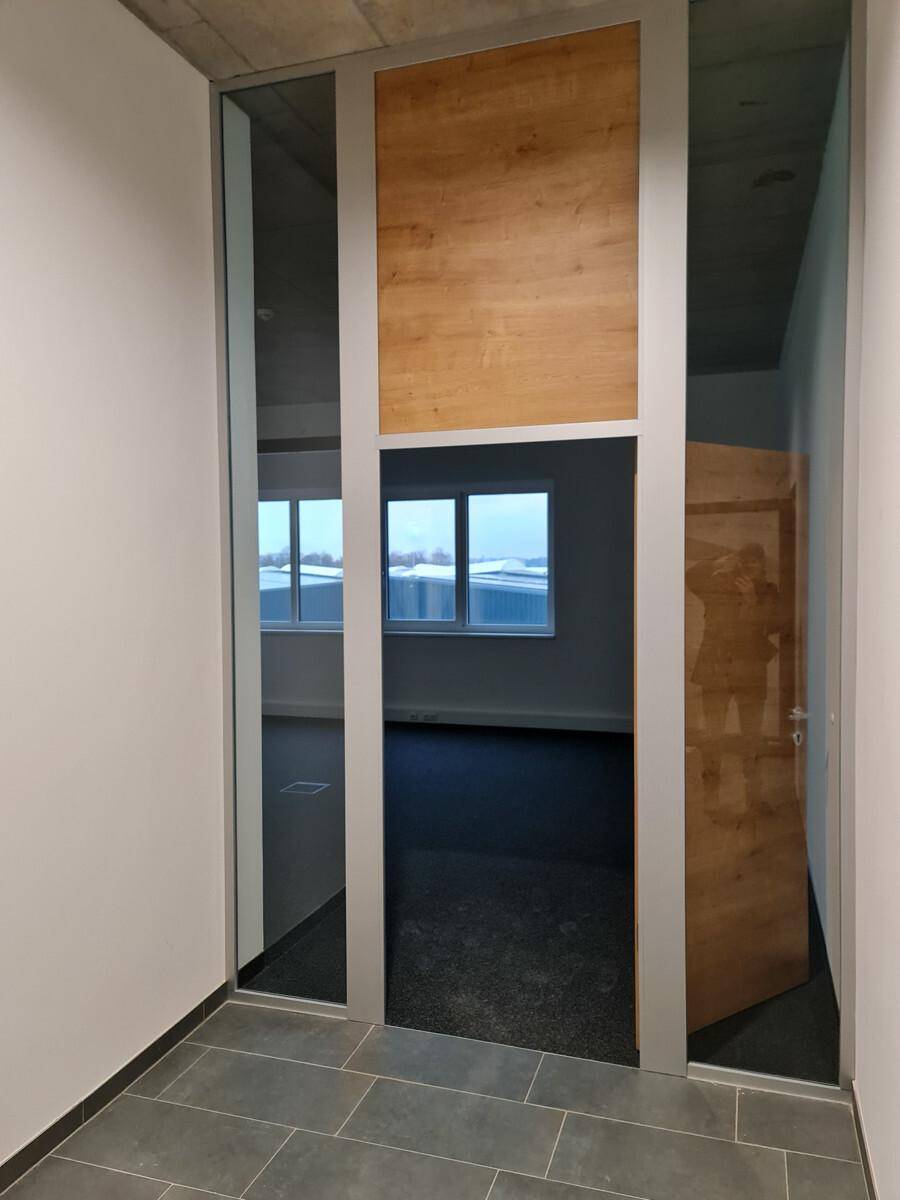 Moderner Flur mit grauen Fliesen, Holzelementen und Blick in ein angrenzendes Büro.