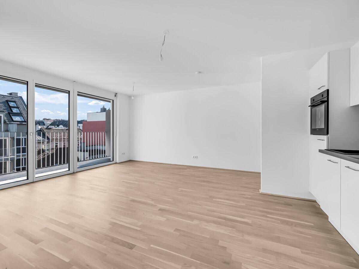 Offener Wohnbereich mit integrierter Küchenzeile, Holzboden und Zugang zu einem Balkon.