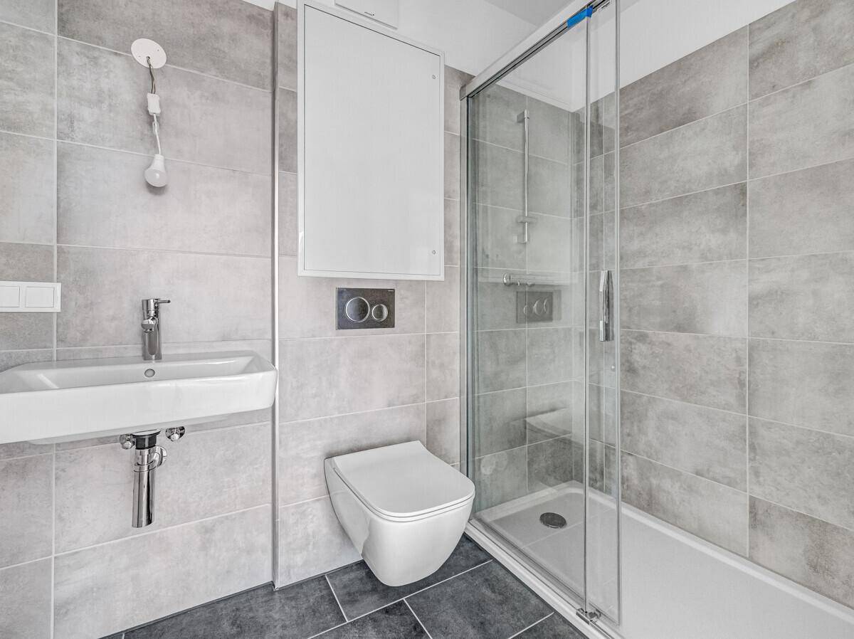 Modernes Badezimmer mit grauen Fliesen, wandhängendem WC und Duschkabine.