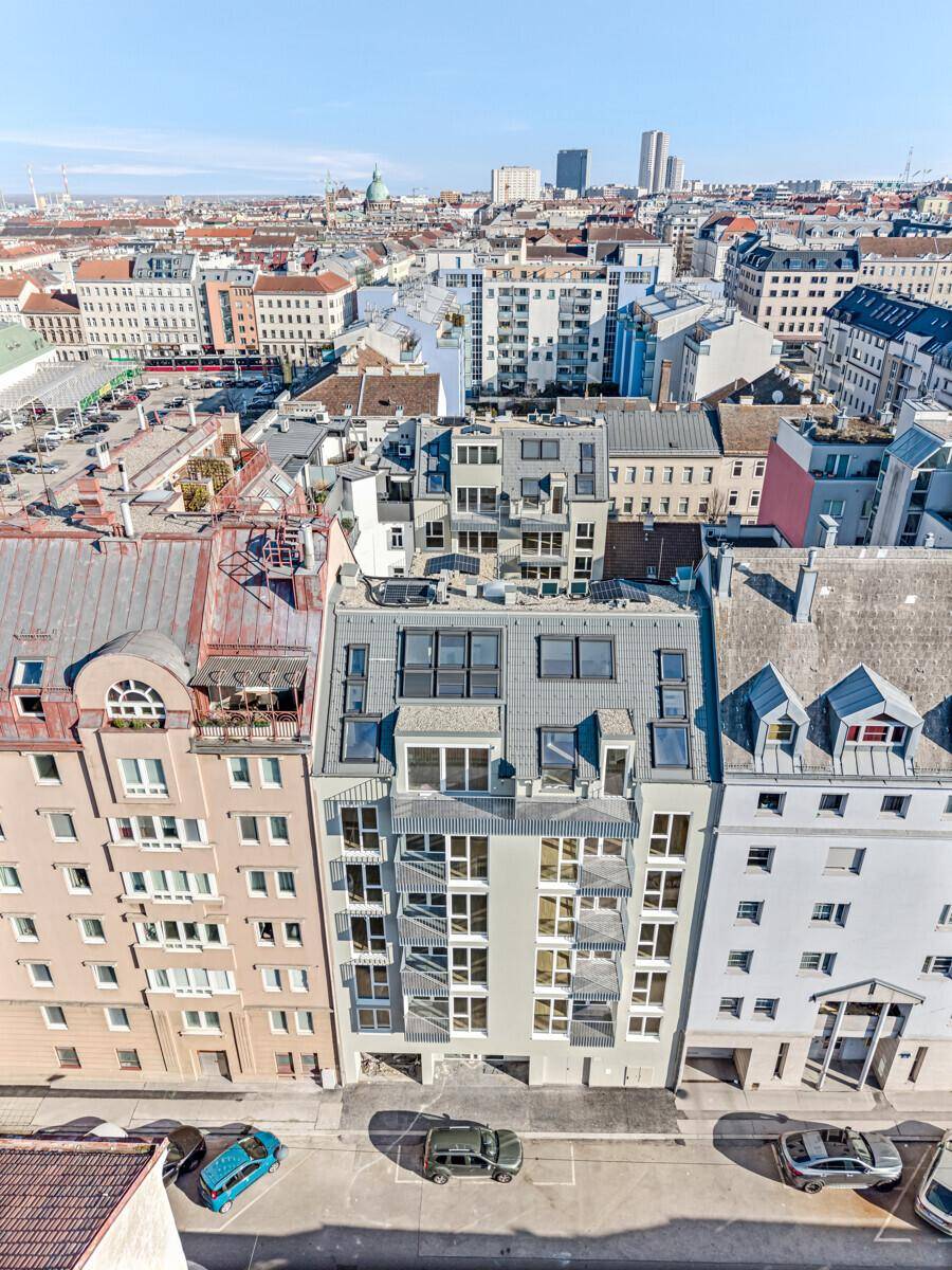 Luftaufnahme eines modernen Wohngebäudes in der Stadt mit umliegenden Dächern und urbaner Landschaft.