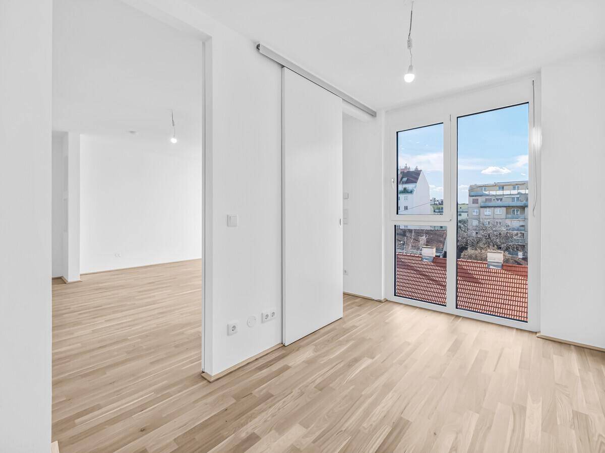 Heller, leerer Raum mit Holzboden, Schiebetüren und Zugang zu einem Balkon mit Stadtblick.
