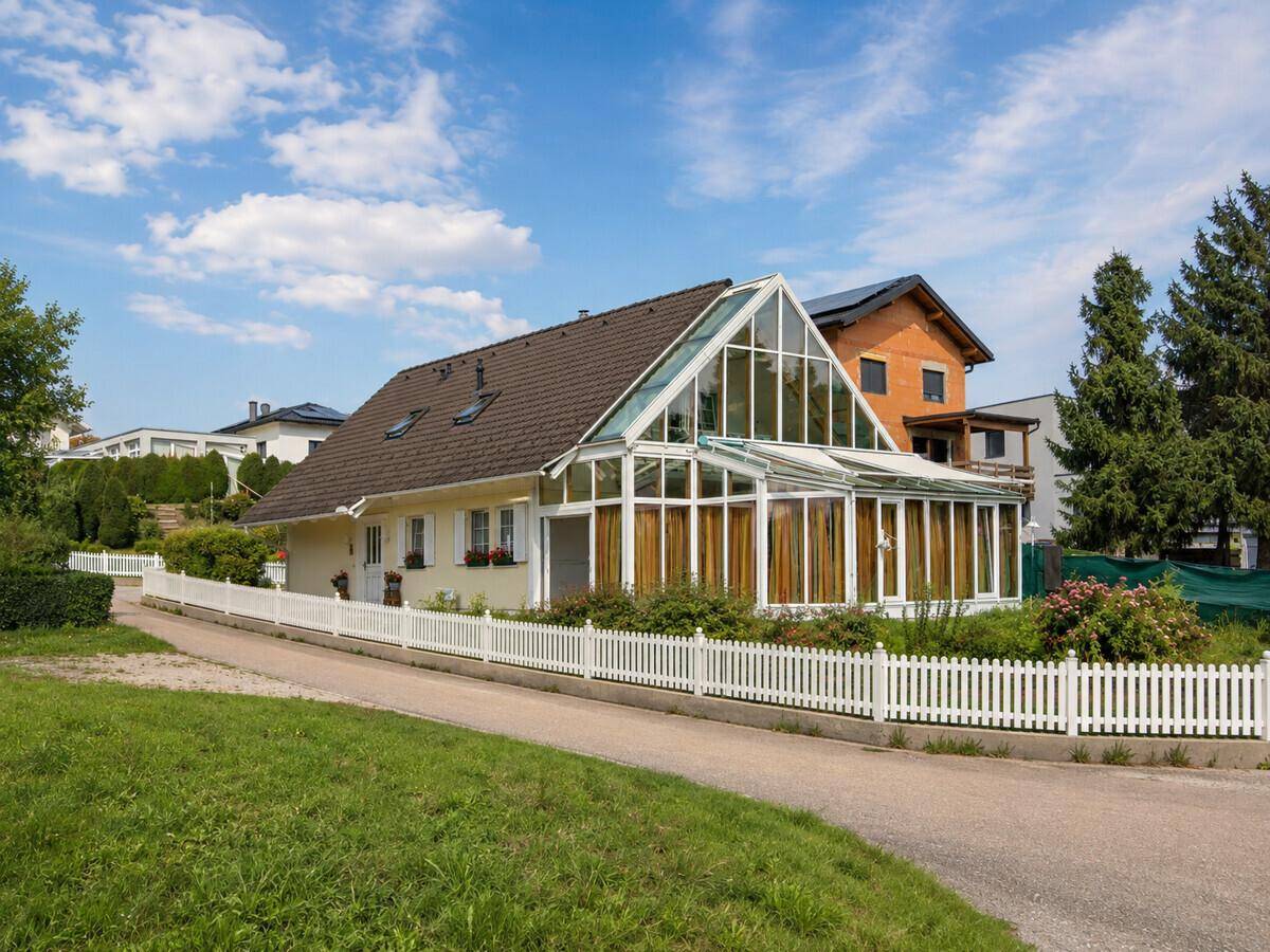 Charmantes Einfamilienhaus mit großem Wintergarten und weißem Lattenzaun in ländlicher Umgebung.