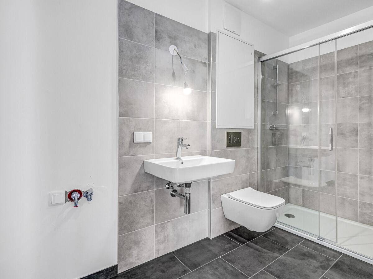 Modernes Badezimmer mit grauen Fliesen, wandhängendem WC und Duschkabine.