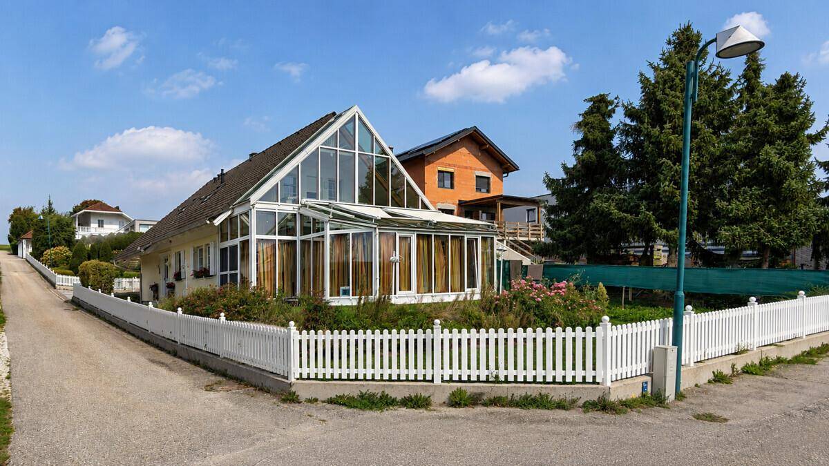 Einfamilienhaus mit weitläufigem Wintergarten und traditionellem Lattenzaun unter blauem Himmel.
