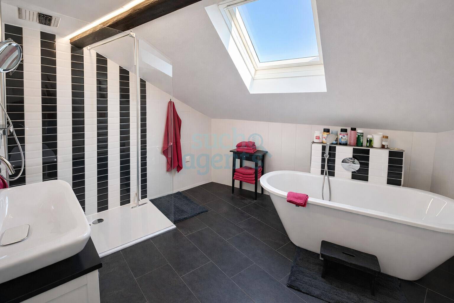 Ein modernes Badezimmer im Dachgeschoss mit freistehender Badewanne, Dusche und Dachfenster.