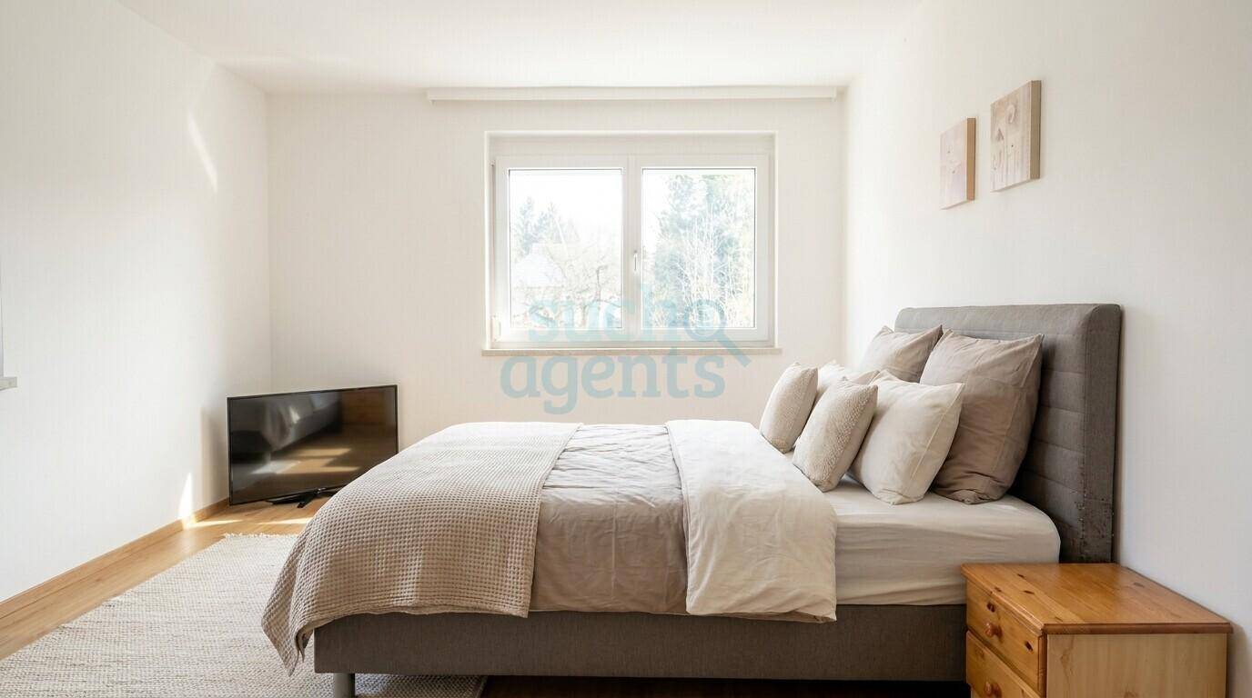 Helles Schlafzimmer mit Doppelbett, Holzfußboden und einem Fenster mit Blick ins Grüne.
