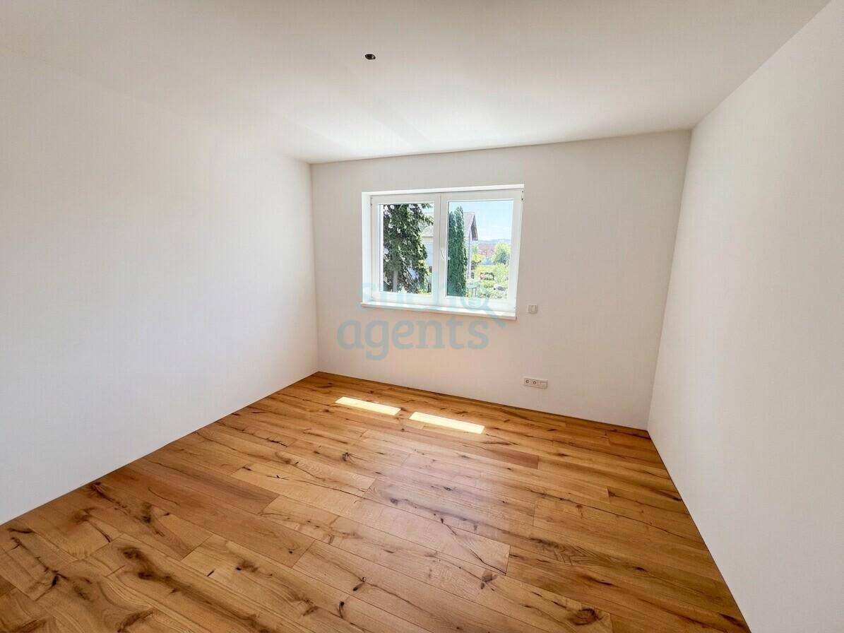 Leeres Zimmer mit Holzboden und großem Fenster, ideal als Schlaf- oder Arbeitszimmer nutzbar.