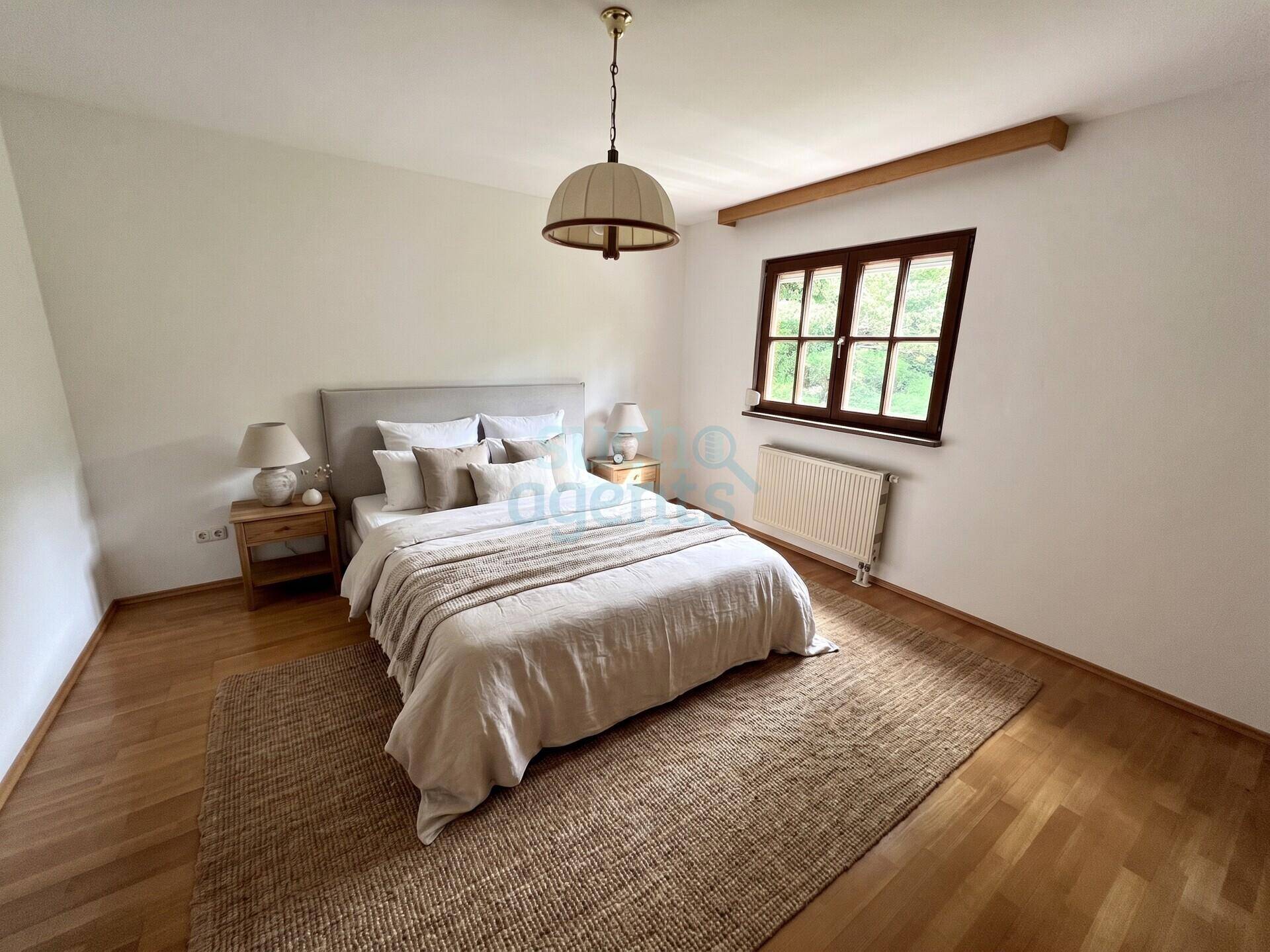Gemütliches Schlafzimmer mit Holzboden, großem Bett und einem Fenster mit Blick ins Grüne.