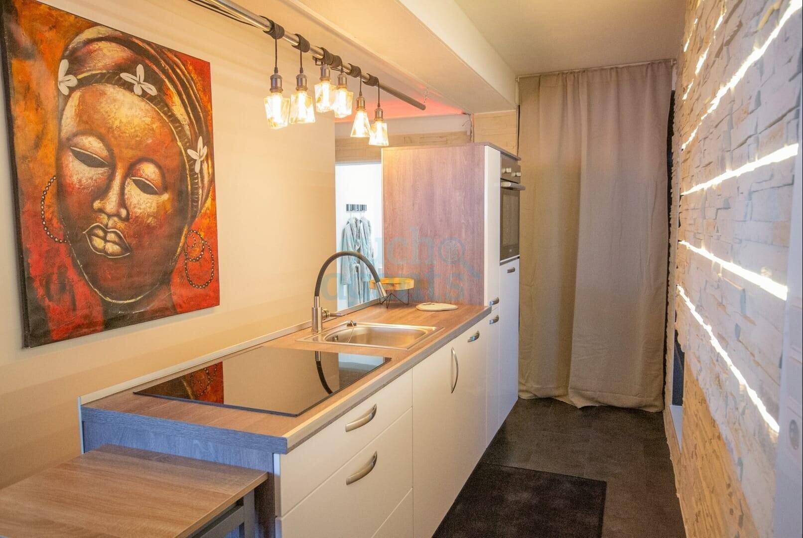 Moderne Küchenzeile mit Induktionskochfeld, Backofen und stilvoller Beleuchtung.