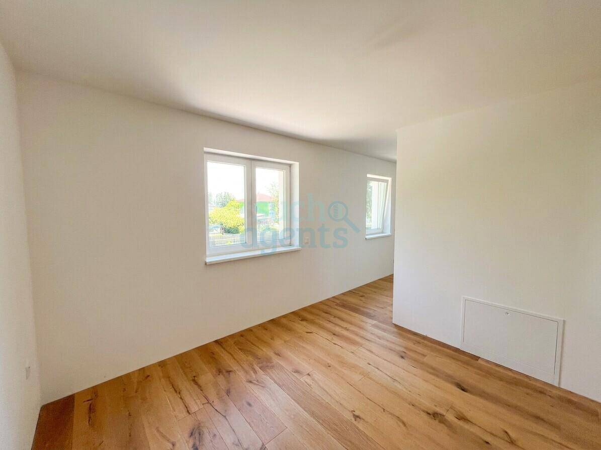 Heller Flur mit Holzboden und mehreren Fenstern, die viel Tageslicht hereinlassen.