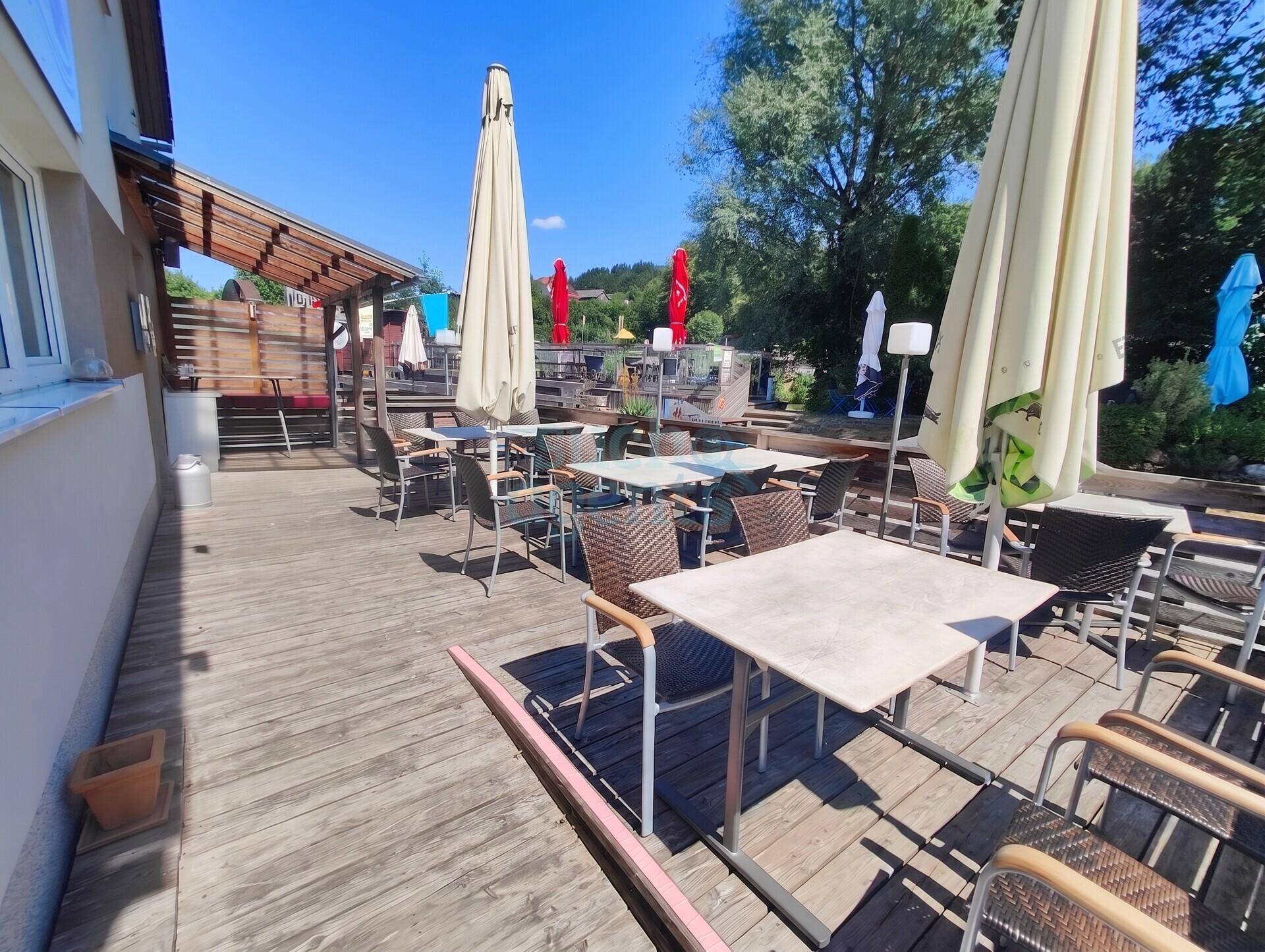 Große Holzterrasse mit zahlreichen Tischen und Stühlen, ideal für den Außenbereich eines Restaurants.